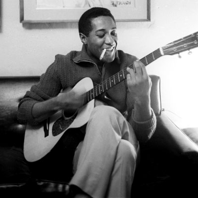 Sam Cooke seated, smiling, holding an acoustic guitar.